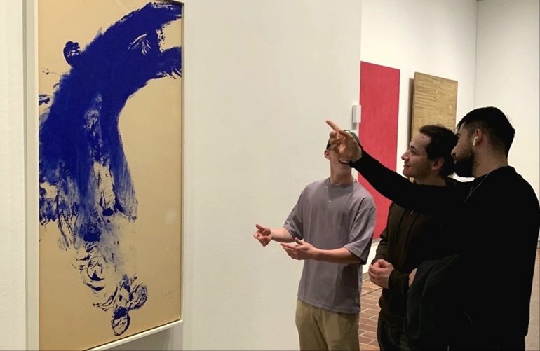 tre elever som pekar på en tavla med blåa penseldrag.