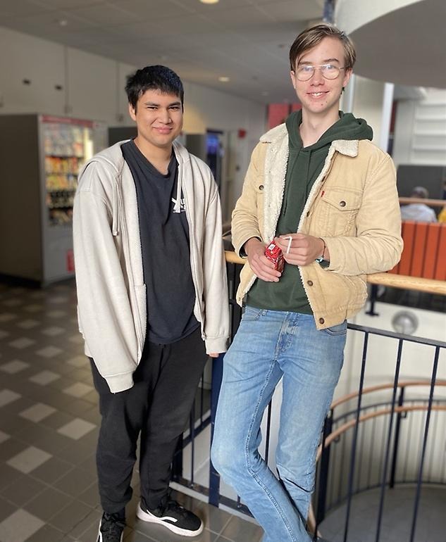 Två elever som lutar sig mot ett trappräcke och ler mot kameran.